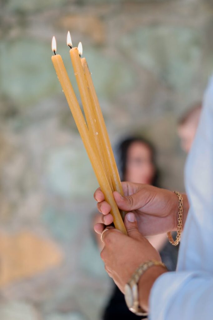 A close-up of a hand holding three lit, long candles during a spiritual ceremony indoors.